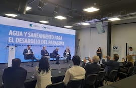 Cuatro panelistas, tres hombres en traje y una mujer con documento, discuten sobre saneamiento en un ambiente formal con público atento.