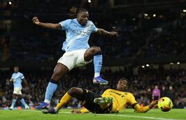 El delantero belga Jeremy Doku salta para evitar la entrada del zaguero colombiano Yerson Mosquera, del Wolves, durante el partido que el Manchester City ganó 2-0. (AFP)}.
