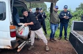 Hombre central carga un saco con logo de Cruz Roja, rodeado de policías en un entorno rural y barroso.