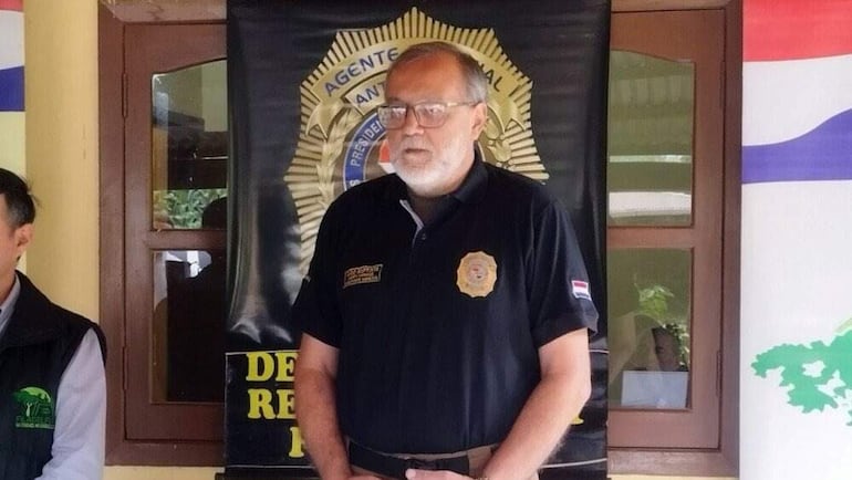 Hombre canoso en camisa negra habla en una mesa con escudo de la Policía Nacional y cartel del Departamento de Prevención.