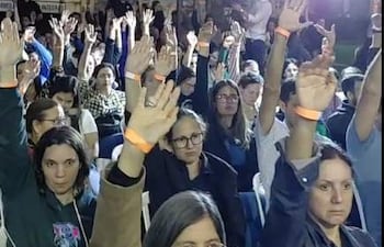 Grupo de médicos levantando las manos en apoyo durante un evento, con expresiones de tranquilidad y preocupación.