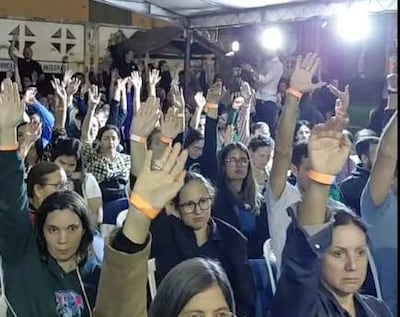 Grupo de médicos levantando las manos en apoyo durante un evento, con expresiones de tranquilidad y preocupación.