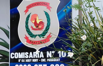Cartel de la Policía Nacional de Paraguay con escudo, en la Comisaría N° 107, rodeado de plantas en un entorno urbano.