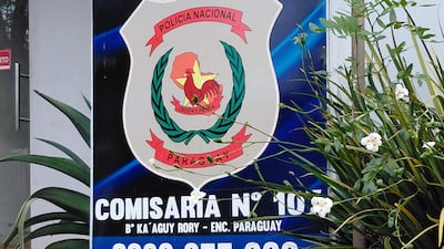 Cartel de la Policía Nacional de Paraguay con escudo, en la Comisaría N° 107, rodeado de plantas en un entorno urbano.
