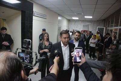 Miguel Prieto en camisa blanca habla a la prensa, mujer con blusa oscura escucha y hombre de traje lo apoya en un ambiente judicial.