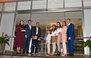 Grupo de ocho personas posando felices en la inauguración del edificio, con lazo tricolor al fondo y vestimenta variada.