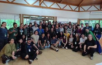 Aproximadamente 50 personas en un ambiente interior, todas sonrientes, algunas con camisetas variadas y credenciales visibles.