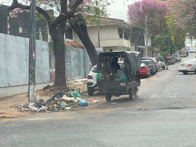 Persona dentro de vehículo de tres ruedas rodeada de basura y autos en una calle de Asunción.