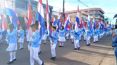 Niños de la Escuela Santa María de los Ángeles marchan en filas con banderas paraguayas en un desfile.