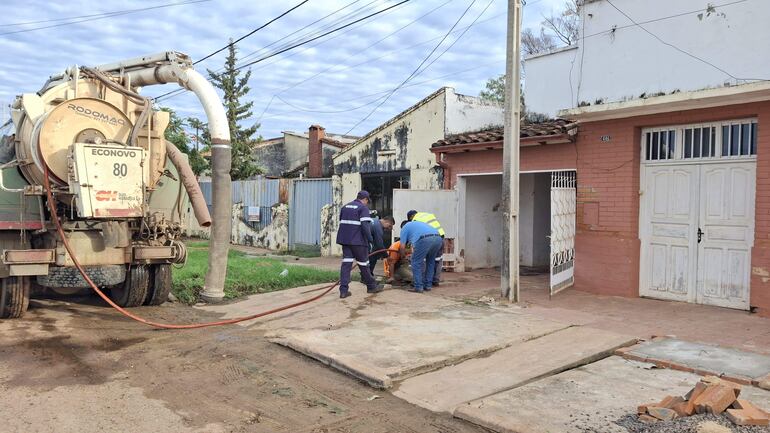 Cuatro trabajadores en uniforme colaboran cerca de una camioneta de servicios, en un ambiente urbano con señal de actividad reciente.