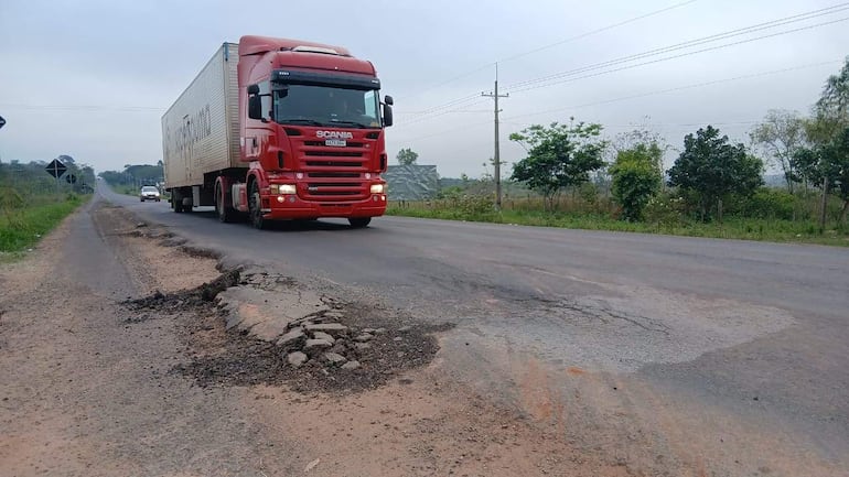 Camión Scania rojo en un camino rural con baches y vegetación a los lados, sin personas visibles.