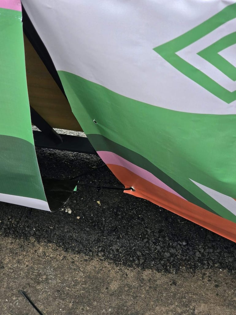 Banner deteriorado en el asfalto, predominando colores verde, blanco y rosa, sin textos visibles ni figuras humanas.