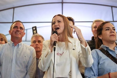 Soledad Núñez con blazer blanco y micrófono, sonriente, rodeada de Rafael Filizzola y Johanna Ortega en un evento interior.