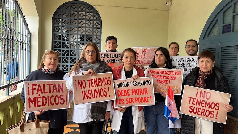 Syrley Ferreira y Marlim Riveros Pesoa en protesta, llevando camisetas blancas y rojas, sosteniendo carteles con mensajes de reclamo.