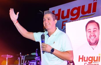 Hugo Carlac, con camiseta celeste, sostiene un micrófono mientras saluda a la audiencia en un ambiente festivo.