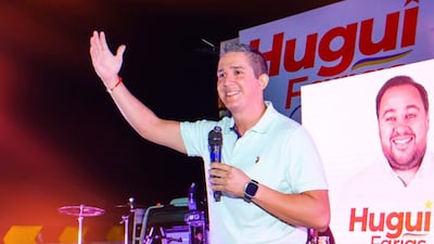 Hugo Carlac, con camiseta celeste, sostiene un micrófono mientras saluda a la audiencia en un ambiente festivo.