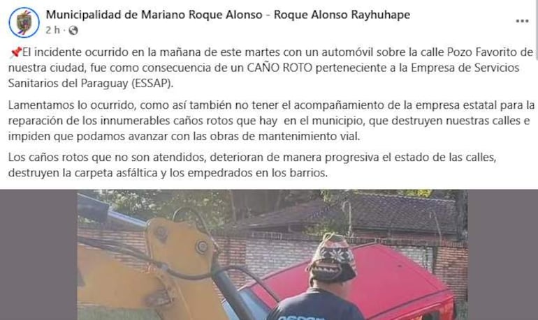 Hombre con casco de pie junto a una retroexcavadora en un entorno urbano, realizando reparaciones en la calle.