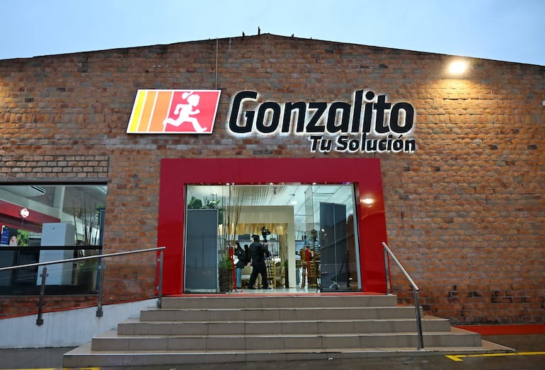 Fachada del negocio Gonzalito con letrero iluminado en rojo y amarillo, escaleras y pared de ladrillo expuesto.
