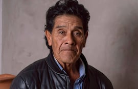 Osvaldo Pitoé de pie en chaqueta de cuero negra, sosteniendo una pintura, con un fondo sencillo y acogedor.