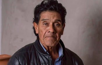 Osvaldo Pitoé de pie en chaqueta de cuero negra, sosteniendo una pintura, con un fondo sencillo y acogedor.