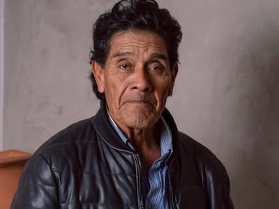 Osvaldo Pitoé de pie en chaqueta de cuero negra, sosteniendo una pintura, con un fondo sencillo y acogedor.