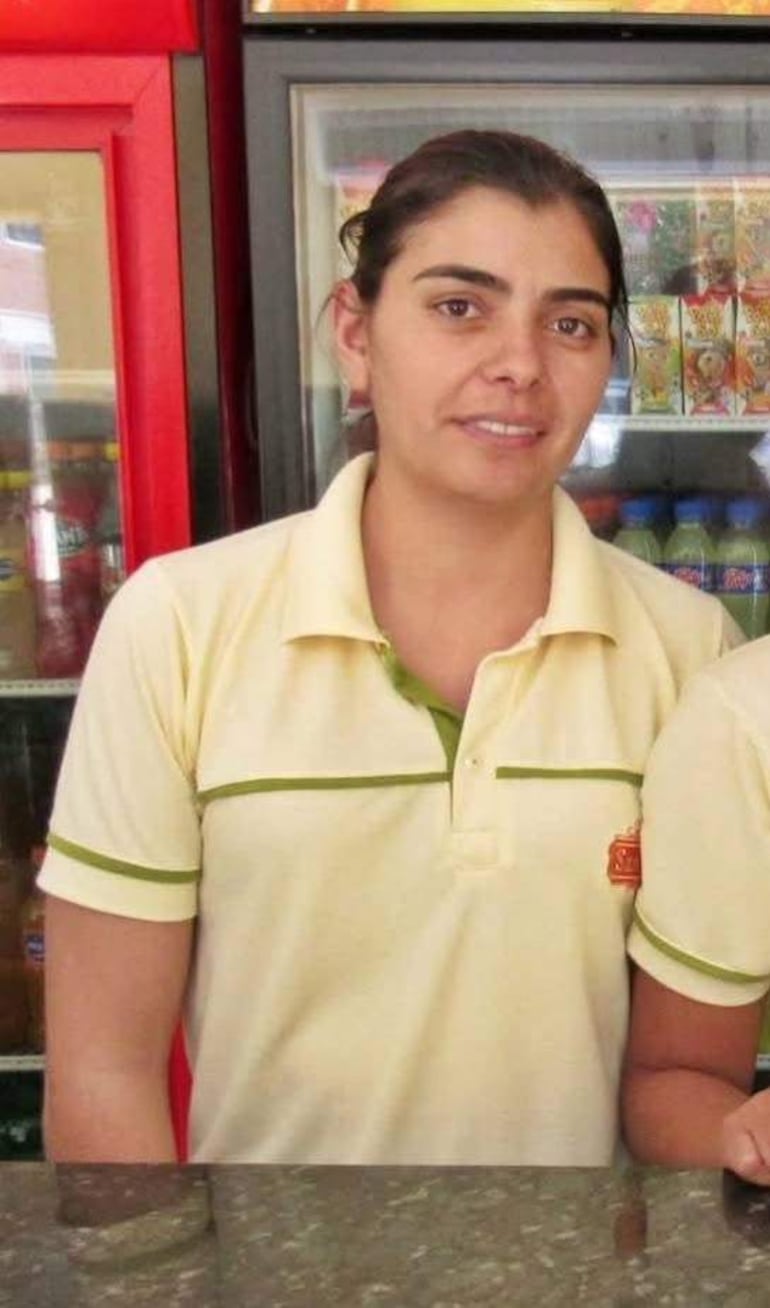 María Liz Cañete de pie frente a un mostrador, luciendo camiseta amarilla con detalles verdes en un ambiente tranquilo.