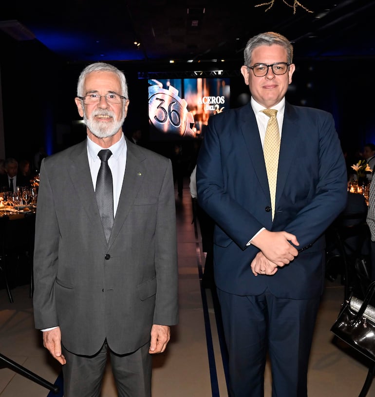 José Antonio Marcondes de Carvalho, con traje gris y sonrisa, posando junto a un hombre con gafas y traje azul oscuro en evento formal.