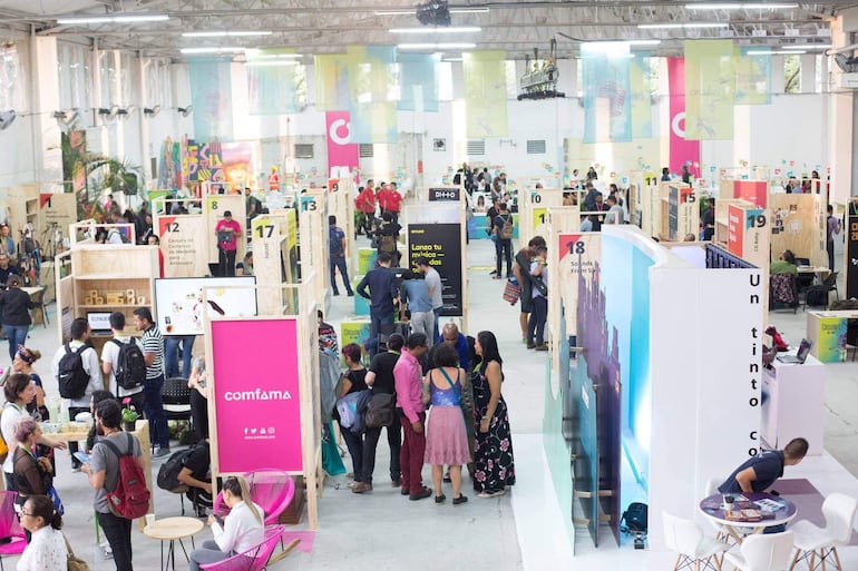 Cientos de personas en un espacio interior, interactuando con stands brillantes y coloridos en un ambiente dinámico y colaborativo.