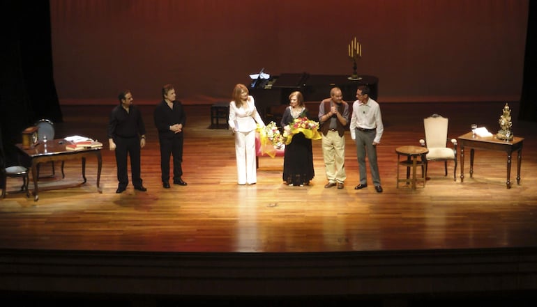 Antonio Grimau en el centro, rodeado de cinco artistas. Fondo oscuro y decorativos en un escenario de madera. Todos expresan alegría.