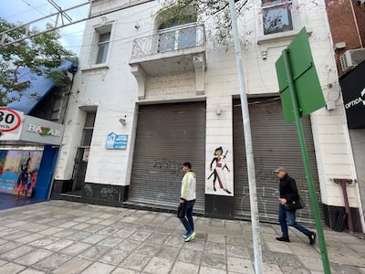 Dos hombres, uno con chaqueta blanca y otro de negro, caminan en una calle desierta con un mural de fondo.