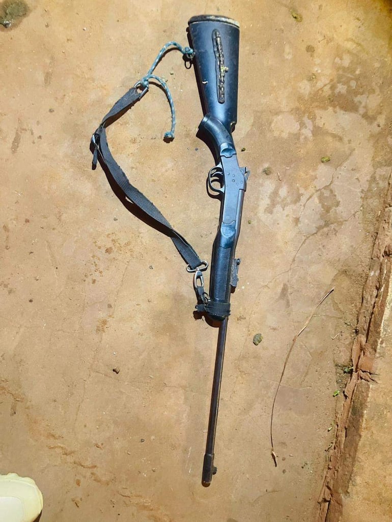Rifle de caza negro con cartucho visible, apoyado en suelo marrón del entorno rústico, sin personas presentes.