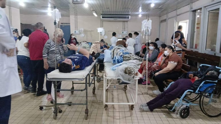 Pacientes en camillas y sillas, algunos con mascarillas, mientras médicos en batas blancas realizan asistencia médica.