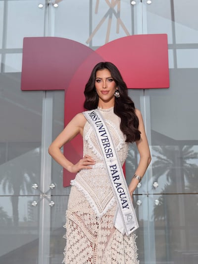 Gretha Matiauda sonríe vestida con un elegante vestido de encaje claro y banda de Miss Universo Paraguay, en un entorno moderno.