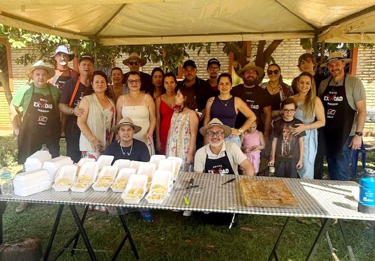 Grupo de personas bajo carpa disfrutando de la jornada, con un hombre en delantal 'EXPLORE PARAGUAY' y niños presentes.