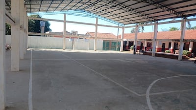 Cancha deportiva techada y vacía con suelo de cemento, iluminada por luz natural y portería de fútbol al fondo.