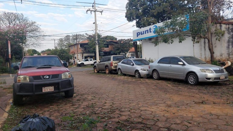 Varios coches estacionados en una calle pavimentada junto a un depósito incendiado, sin presencia de personas.