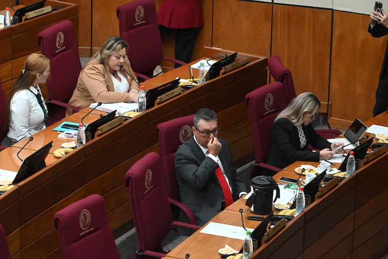 Zenaida Delgado en blusa blanca y lazo negro, Gustavo Leite en traje gris, conversando en un entorno legislativo con documentos sobre la mesa.