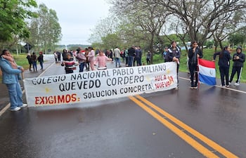 Manifestantes con abrigos sostienen una pancarta en la carretera, mientras una mujer con abrigo claro toca un tambor.