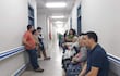 Grupo de personas en pasillo de IPS de Benjamín Aceval, algunas sentadas y otras de pie, con expresión tranquila y cansada.