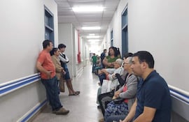 Grupo de personas en pasillo de IPS de Benjamín Aceval, algunas sentadas y otras de pie, con expresión tranquila y cansada.