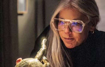 Laura Mandelik, con cabello rubio y gafas grandes, inclina su cuerpo hacia un objeto dorado iluminado en un entorno oscuro.