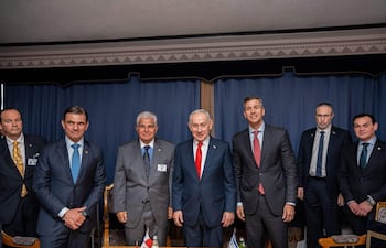 Peña en traje oscuro con corbata amarilla, rodeado de hombres en trajes, todos frente a un fondo azul, con expresiones tranquilas y felices.