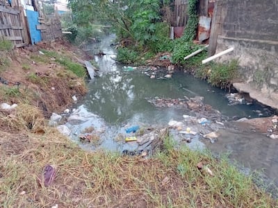 Cuerpo de agua contaminado en barrio San Miguel, con basura visible en la superficie y terreno descuidado alrededor.