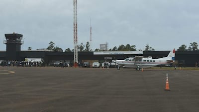 Aeropuerto con un avión estacionado y una multitud esperando, bajo un cielo nublado y con vehículos en la zona.