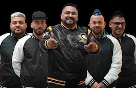 Cinco hombres de la Agrupación Marilyn sonríen y gesticulan, vestidos con chaquetas negras y blancas con detalles amarillos, sobre un fondo negro.