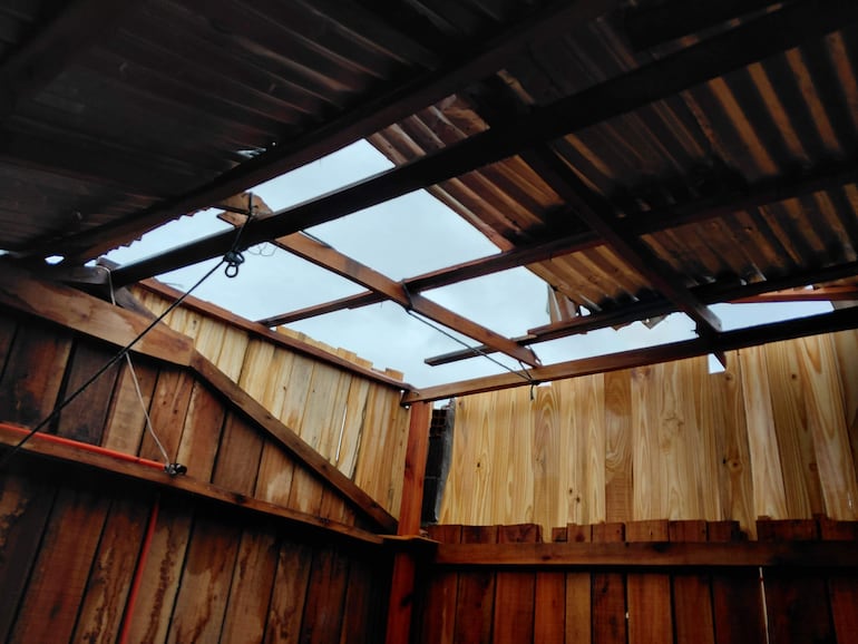 Interior de una vivienda destechada, con vista al cielo nublado y paredes de madera deteriorada.