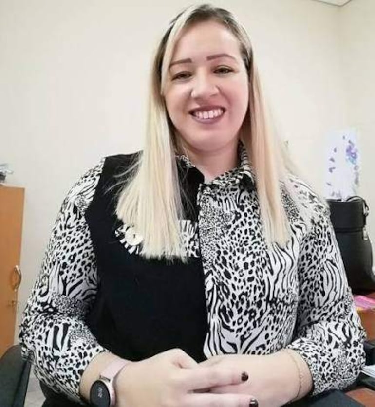 Mujer con cabello rubio y camisa de cebra, sonríe en una oficina con mobiliario visible.