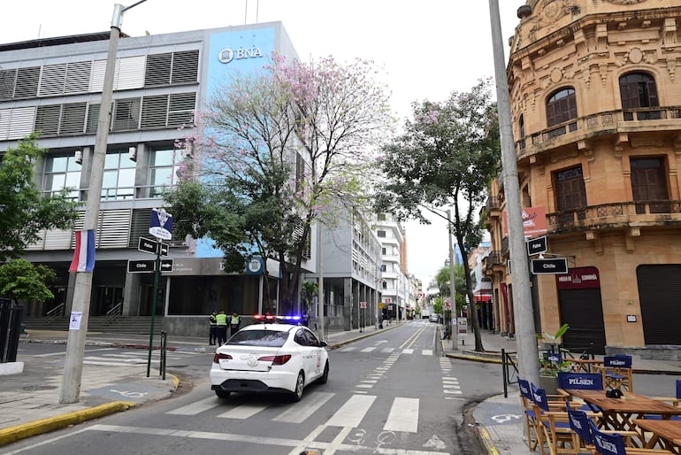 Agentes de seguridad en uniforme frente a un edificio moderno, con un vehículo policial estacionado en la calle deteriorada.