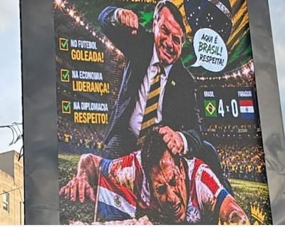 Jair Bolsonaro de pie en traje formal celebra mientras otro arrodillado con camiseta paraguaya escucha el mensaje en un cartel sobre fútbol.