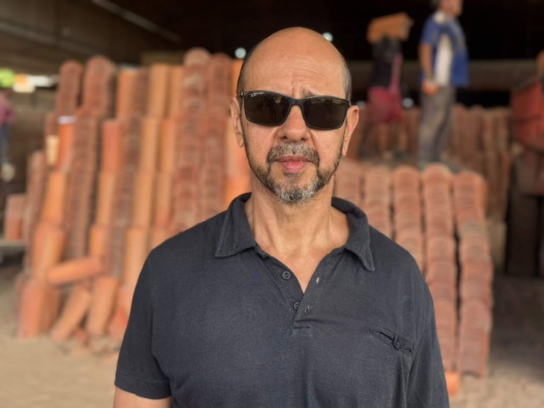 Hombre con gafas de sol en un taller de cerámica, mostrando seriedad mientras observa pilas de terracota en el fondo.